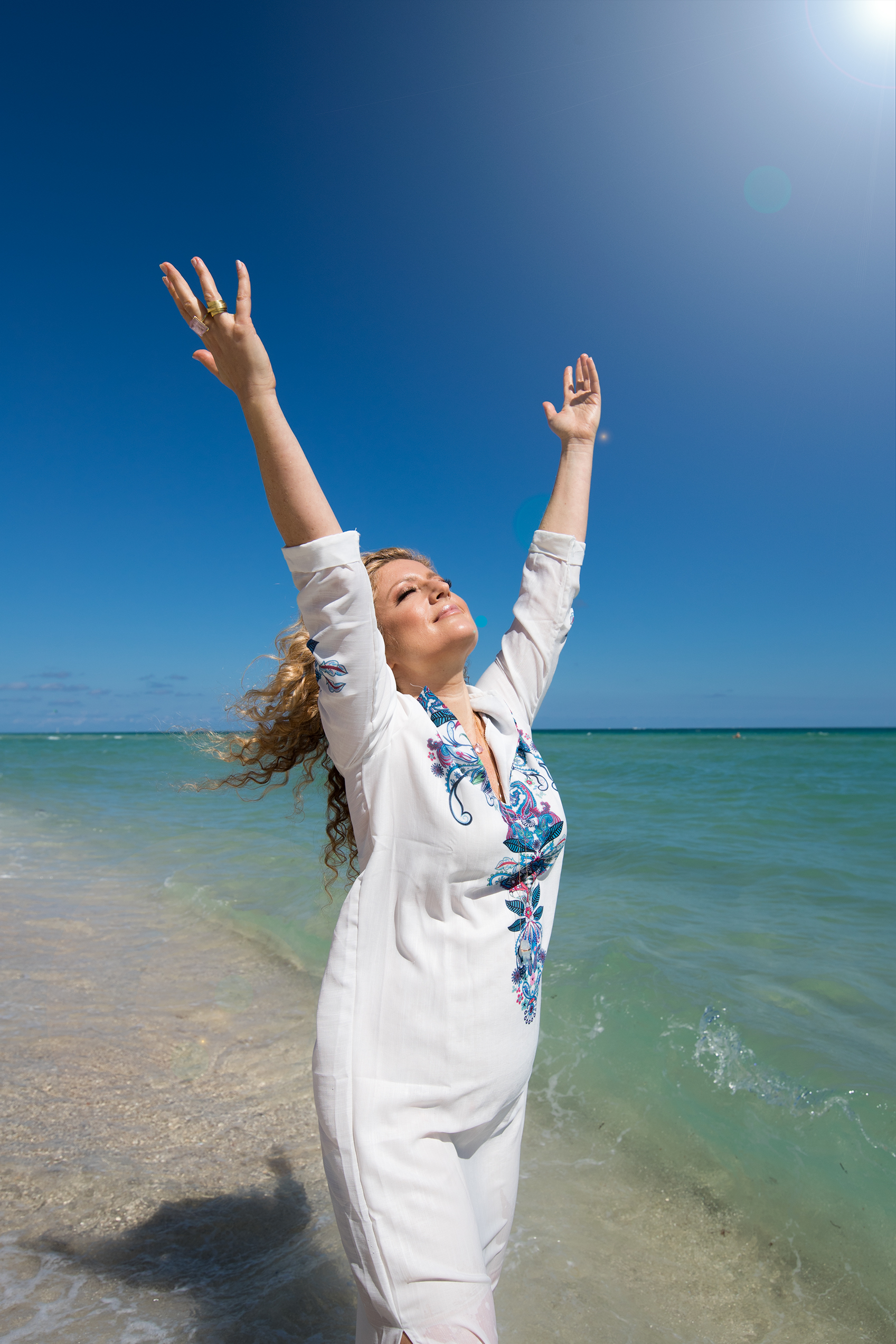 Woman in a white dress on the beach with raised arms